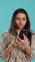 Vertical Indian woman swiping on smartphone touchscreen to answer phone call from friend, isolated over studio background. Portrait of person listening and agreeing with mate during telephone call, camera A video