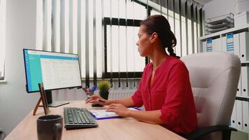 Hispanic young woman sitting in office and working on desktop pc. Entrepreneur sitting in front of computer in professional company workspace typing on keyboard looking at monitor writing reports video