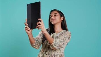 indisch narzisstisch Frau mit Tablette zu nehmen Selfies von alle Winkel. vergeblich Sozial Medien Benutzer nehmen Fotos mit Digital Gerät Selfie Kamera, lächelnd glücklich, Studio Hintergrund, Kamera ein video