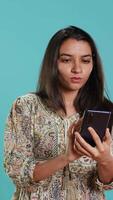 Vertical Indian woman discussing with best friend over telephone call using smartphone. Cheerful person talking with mate in phone call using cellphone, isolated over studio background, camera A video