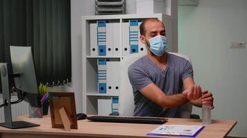 imprenditore con maschera digitando su computer seduta nel nuovo normale posto di lavoro. libero professionista Lavorando nel moderno ufficio spazio di lavoro pulizia mani utilizzando espurgare alcool gel contro corona virus video