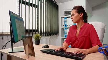 Hispanic woman employee checking appointments on computer sitting in modern office room. Entrepreneur working in professional company workspace typing on computer keyboard looking at desktop video