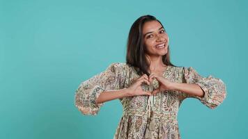 retrato de sonriente amoroso mujer haciendo corazón símbolo forma gesto con manos, demostración amabilidad. contento cariñoso Novia haciendo oferta amor gesticulando para novio, estudio fondo, cámara un video