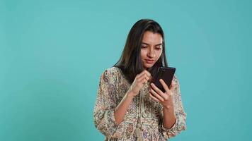 Woman happily scrolling on phone touchscreen to check social media feed, amazed by photo. Indian person browsing internet websites, astonished by content, studio background, camera A video