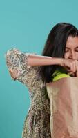 Vertical Woman with recycled paper bag in hands filled with vegetables testing quality, studio background. Sustainable living person inspecting groceries after doing purchases in shop, camera A video