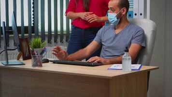 Business people wearing protective mask in new normal office making strategy. Team working in profesional workspace in corporate company typing on computer keyboard looking and pointing at desktop. video