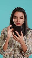 Vertical Woman scrolling on smartphone screen, doing online shopping, amazed by beautiful clothes. Portrait of relaxed person browsing internet websites, exclaiming in astonishment, studio background, camera A video