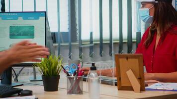 desinficerande händer med desinfektionsmedel gel Sammanträde på skrivbord i ny vanligt kontor med social avståndstagande. arbetare arbetssätt i modern arbetsplats respekterar skydd regler mot covid virus använder sig av plexiglas video