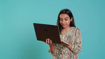 kvinna komponera e-post, försiktigt skriver på bärbar dator tangentbord, kämpar till tror av Vad till skriva. indisk person sändning post uppkopplad, brainstorming meddelande aning, studio bakgrund, kamera en video