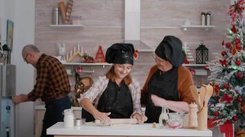 glücklich Familie feiern traditionell Weihnachten Urlaub vorbereiten Lebkuchen Kekse im kulinarisch dekoriert Weihnachten Küche. Enkel tragen Kochen Schürze Herstellung hausgemacht Teig mit rollen Stift video