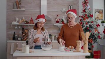 Grandmother explaining how to making traditional dessert dough to granddaughter preparing homemade delicious cookie in culinary decorated kitchen. Happy family enjoying christmas holidays video