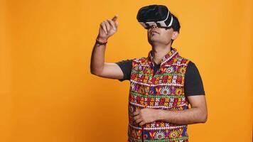 Indien homme portant virtuel réalité casque, Faire balayer gestes. La technologie passionné en utilisant haute technologie futuriste moderne vr gadget, isolé plus de studio arrière-plan, caméra b video