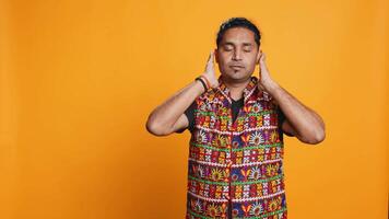 Man wearing traditional indian clothing covering eyes, ears and mouth, imitating three wise monkeys, doing dont see, dont hear and dont speak hand gesturing concept, studio background, camera B video