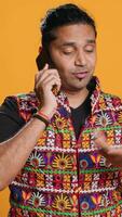 Vertical Man discussing with best friend over telephone call, enjoying leisure time. Upbeat person wearing indian attire talking with mate in phone call, isolated over studio backdrop, camera A video
