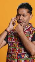 Vertical Indian man discussing with best friend over telephone call using smartphone. Cheerful person talking with mate in phone call using cellphone, isolated over studio background, camera A video