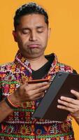 Vertical Man shakes head in disbelief after realizing lack of necessary funds while trying to shop online on tablet. Disappointed indian person gets credit card transaction rejected, studio backdrop, camera A video