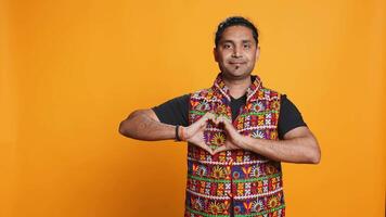 Portrait of jolly friendly indian man doing heart symbol shape gesture with hands. Cheerful nurturing person showing love gesturing, isolated over studio background, camera B video