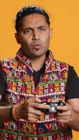 Vertical Gamer annoyed after losing online multiplayer videogame, being defeated by rival players. Indian man shocked and gutted after seeing game over message, holding controller, studio background, camera A video