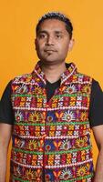 Vertical Portrait of optimistic indian man wearing colorful vest with positive facial expression smiling, looking pleased. Calm person in traditional clothing, feeling satisfied, studio backdrop, camera B video