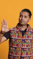 Vertical Indian man trying to stop chaotic fight using calming hand gesture to diffuse tensions, doing peaceful resolution. Reassuring person doing calm down sign gesturing, studio background, camera A video