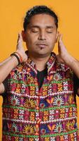 Vertical Man wearing traditional indian clothing covering eyes, ears and mouth, imitating three wise monkeys, doing dont see, dont hear and dont speak hand gesturing concept, studio background, camera A video