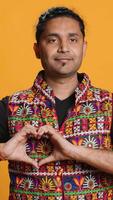 Vertical Portrait of smiling loving man doing heart symbol shape gesture with hands, showing kindness. Happy affectionate person doing tender love gesturing, isolated over studio background, camera A video