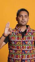 Vertical Indian man doing ok hand sign, feeling pleased, agreeing with satisfactory conclusion. Optimistic person doing okay symbol gesturing, offering positive feedback, studio background, camera A video