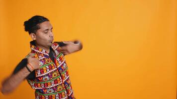 Excited person wearing traditional clothing having fun, dancing on oriental music. Delighted talented man doing entertaining bollywood dance moves, studio background, camera B video