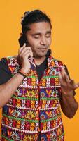 Vertical Man discussing with best friend over telephone call, enjoying leisure time. Upbeat person wearing indian attire talking with mate in phone call, isolated over studio backdrop, camera B video