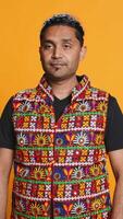 Vertical Portrait of jolly indian man with colorful garment smiling, looking pleased, isolated over studio background. Joyous person in traditional attire feeling carefree, camera B video