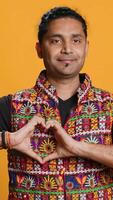 Vertical Portrait of jolly friendly indian man doing heart symbol shape gesture with hands. Cheerful nurturing person showing love gesturing, isolated over studio background, camera A video