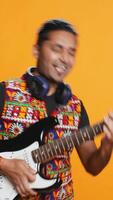 Vertical Happy man holding electric guitar, playing rock music, isolated over studio background. Cheerful indian musician using musical instrument, doing concert, playing songs, camera B video