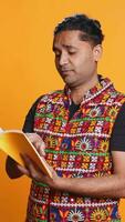 Vertical Indian man reading book, having fun and enjoying characters and plot, isolated over studio background. Relaxed person browsing novel, enjoying leisure time, appreciating literature, camera B video