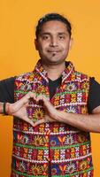 vertikal porträtt av glad vänlig indisk man håller på med hjärta symbol form gest med händer. glad vårda person som visar kärlek gestikulerande, isolerat över studio bakgrund, kamera b video