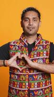 Vertical Portrait of smiling loving man doing heart symbol shape gesture with hands, showing kindness. Happy affectionate person doing tender love gesturing, isolated over studio background, camera B video