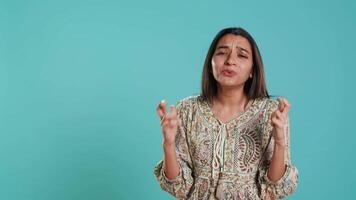 Portrait of upbeat indian woman crossing fingers, making wish, isolated over studio background. Jolly BIPOC person hoping for good luck, waiting for miracle, studio backdrop, camera A video