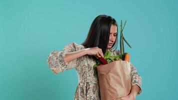 trastornado mujer ceñudo después olvidando a comprar todo, mirando dentro papel bolso con vegetales. consciente vivo persona malhumorado después dándose cuenta algunos comestibles son desaparecido, cámara un video