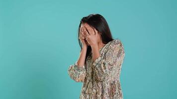 Fearful indian woman covering face with palms, worried about troubling peril, isolated over studio background. Insecure person fearing endangerment, feeling distressed in face of adversity, camera A video