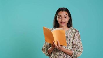 Radiant person reading interesting book, enjoying hobby, being entertained, isolated over studio background. Upbeat woman with novel in arms enjoying relaxation time, reading text aloud, camera A video