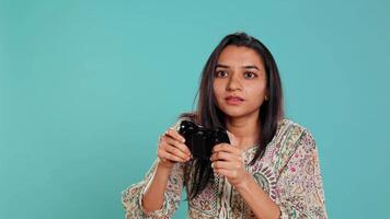 Competitive woman playing videogames with motion controlled controller, studio background. Indian Person participating in internet multiplayer racing game using gyroscope function on gamepad, camera B video