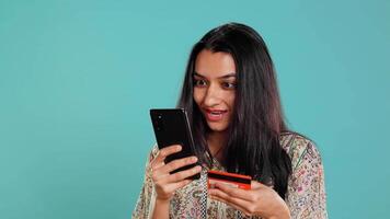 Woman adding payment method on phone website, delighted to take advantage of promotions, studio background. Person thrilled to do internet shopping, typing credit card data on smartphone, camera B video