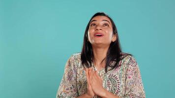 Indian woman putting hands together in begging gesture, making wish, isolated over studio background. Faithful person looking upwards to sky, asking for something, praying and hoping, camera B video