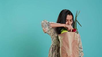 mujer con reciclado papel bolso en manos lleno con vegetales pruebas calidad, estudio antecedentes. sostenible vivo persona inspeccionando comestibles después haciendo compras en comercio, cámara un video