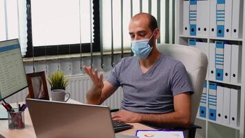 Entrepreneur wearing protection mask using laptop for organizing online conference. Freelancer working in new normal office discussing chatting having virtual meeting, using internet technology video