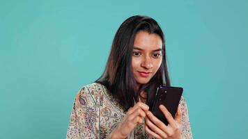 femme Heureusement défilement sur téléphone écran tactile à vérifier social médias alimentation, étonné par photo. Indien la personne navigation l'Internet sites Internet, étonné par contenu, studio arrière-plan, caméra b video