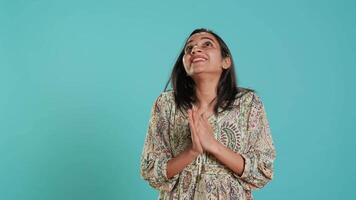 Indisch vrouw zetten handen samen in bedelen gebaar, maken wens, geïsoleerd over- studio achtergrond. trouw persoon op zoek omhoog naar lucht, vragen voor iets, bidden en hopend, camera een video