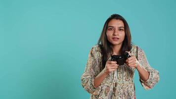 alegre indiano jogador mostrando polegares acima placa gesticulando enquanto segurando controlador depois de ganhando videogame. alegre mulher desfrutando jogos, fazendo aprovando mão gesto, estúdio fundo, Câmera uma video