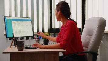 Hispanic freelancer working using clipboard and pc in workplace early in the morning. Entrepreneur sitting on chair in professional company workspace typing on computer keyboard looking at desktop video