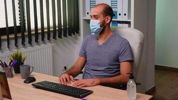 Business man sitting in front of compurer in new normal office having call wearing protection mask. Freelancer discussing chatting during virtual conference, meeting, using internet technology. video