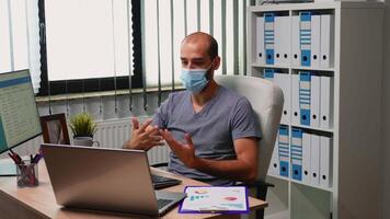 Man with protection face mask using laptop for meeting. Freelancer working in new normal office discussing chatting having virtual online conference, using internet technology video